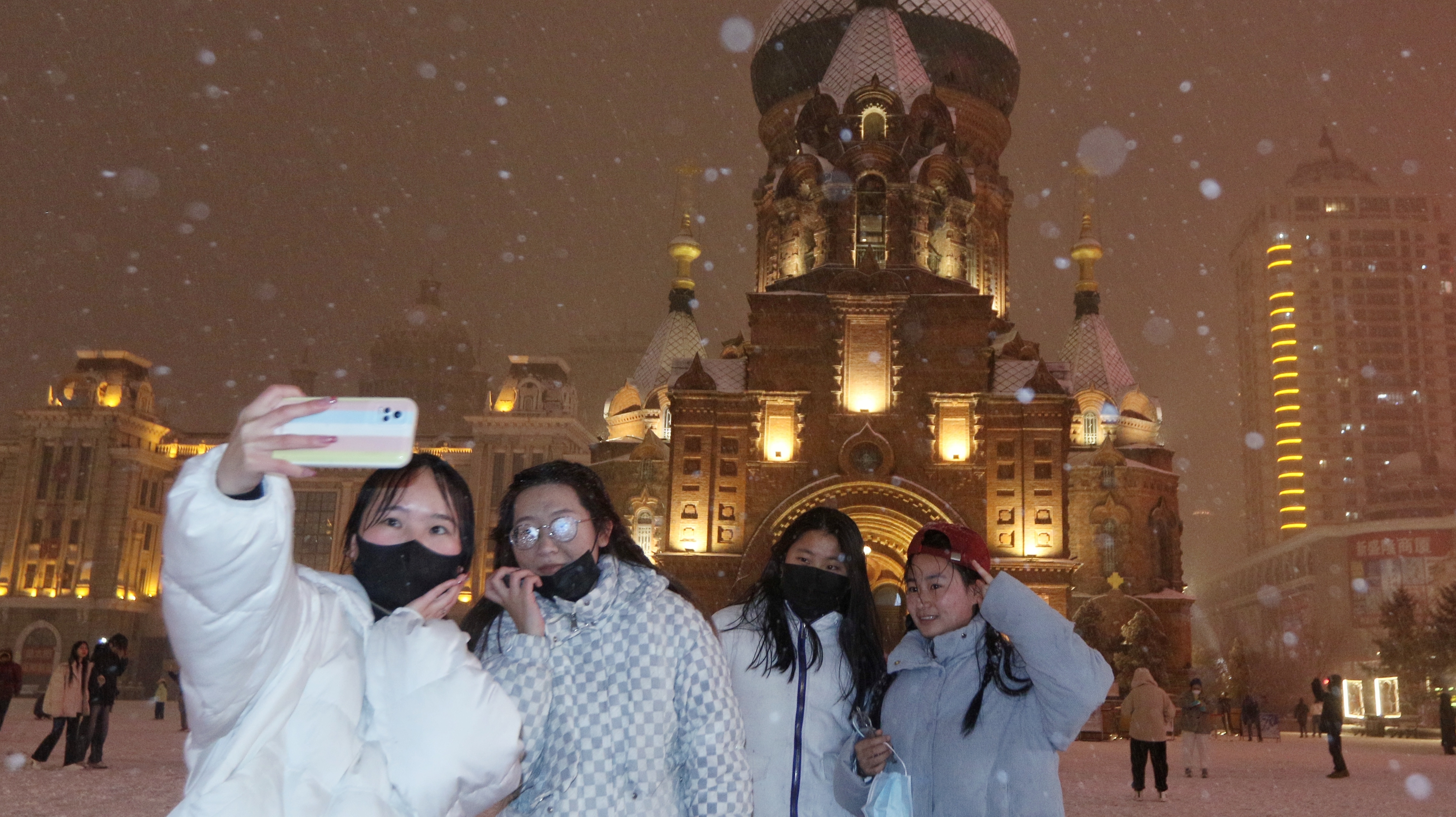 14日晚，冰城哈尔滨再度降雪。纷纷扬扬的雪花在夜色里飞舞，让建筑艺术广场上打卡的游客多了份惊喜。
